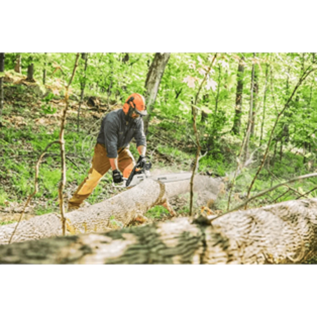 Man wearing protective gear using gas-powered chainsaw to cut fallen tree in dense green forest for home improvement