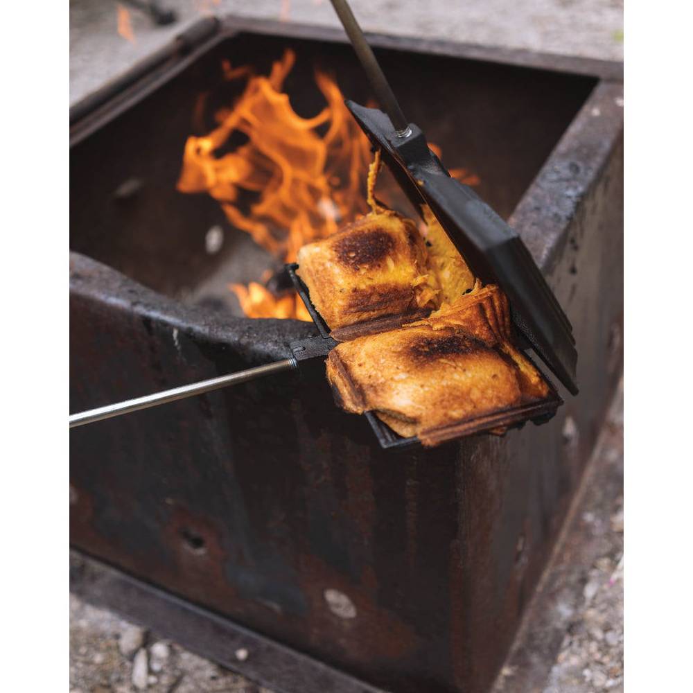 Toasting sandwiches over an open flame using a double cast iron sandwich cooker with long handles outdoors