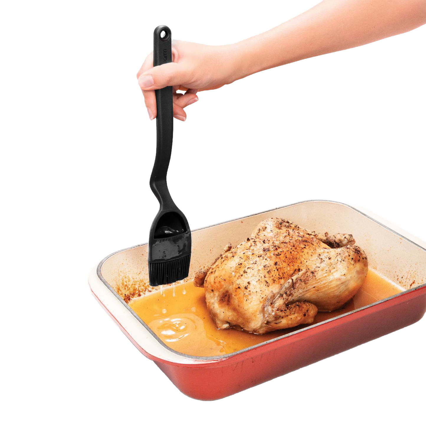 Hand holding black Brizzle Basting Brush with curved handle basting roasted chicken in red roasting pan for kitchen utensils