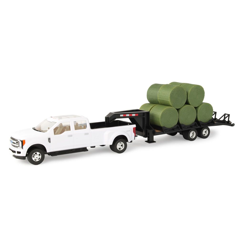White die-cast pickup toy with black trailer carrying six green round bales for farmhouse play or display