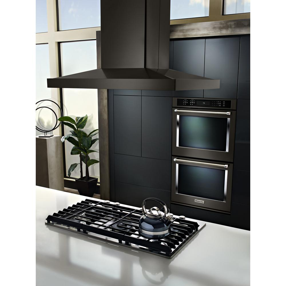 Modern kitchen with black stainless steel gas cooktop and large matte black canopy range hood above white countertop