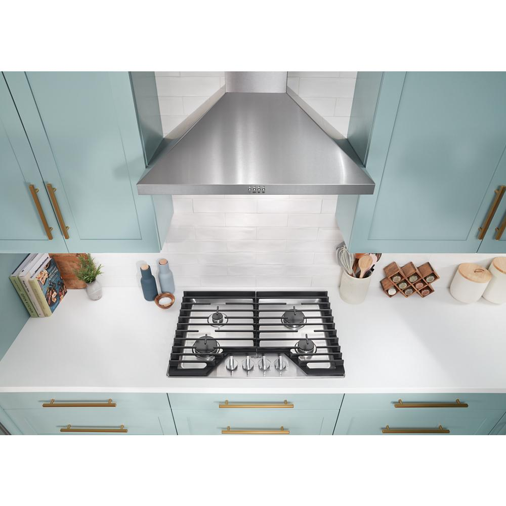 Overhead view of stainless steel gas cooktop with five burners and hinged cast-iron grates in teal kitchen cabinetry