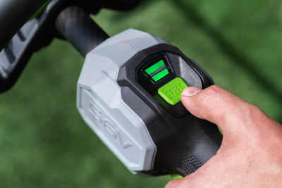 Close-up of hand pressing speed control button on black and gray cordless outdoor power tool handle