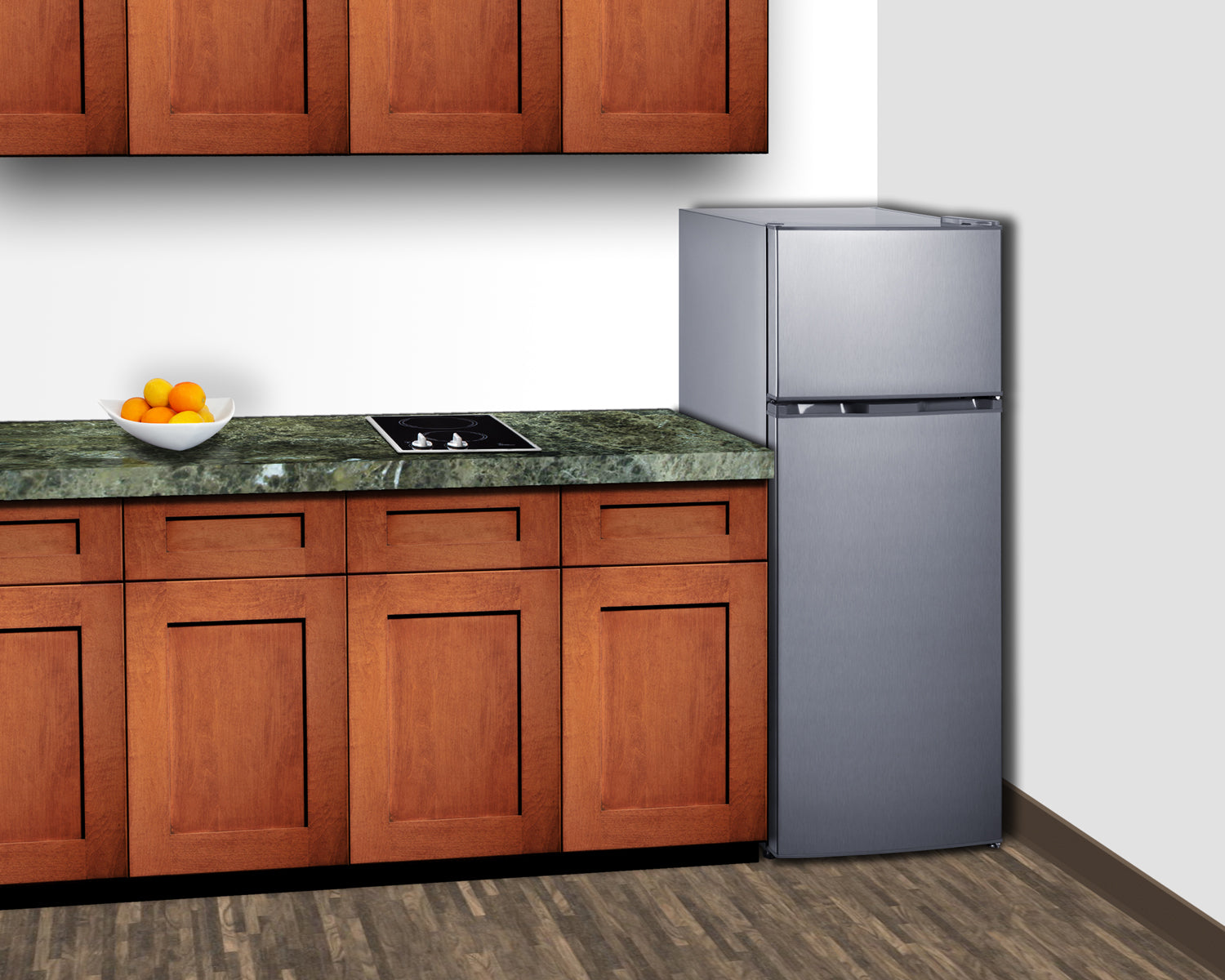 Compact stainless steel top-mount refrigerator-freezer in kitchen setting with wooden cabinetry and green countertop surface