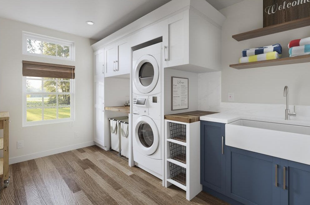 White stack washer and dryer combo installed in bright laundry room with blue lower cabinetry and farmhouse sink