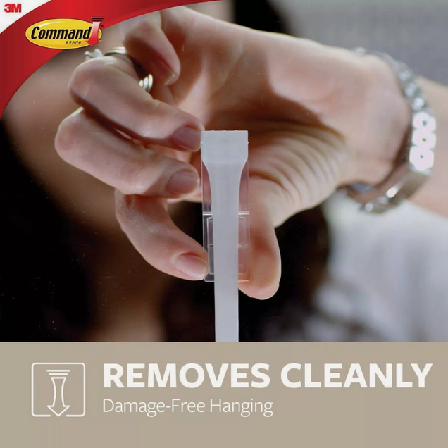 Hand holding clear adhesive strip for damage-free hanging in hardware and fasteners for home improvement tools
