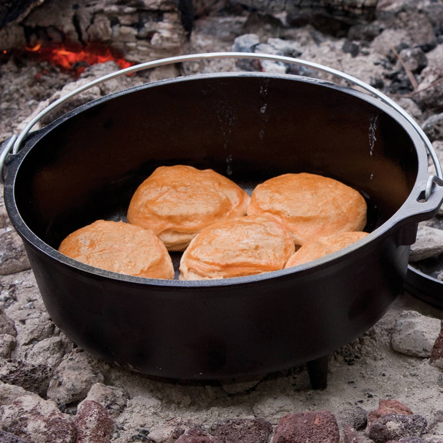 Pre-seasoned cast iron camp Dutch oven with biscuits baking over hot coals in outdoor kitchenware setting