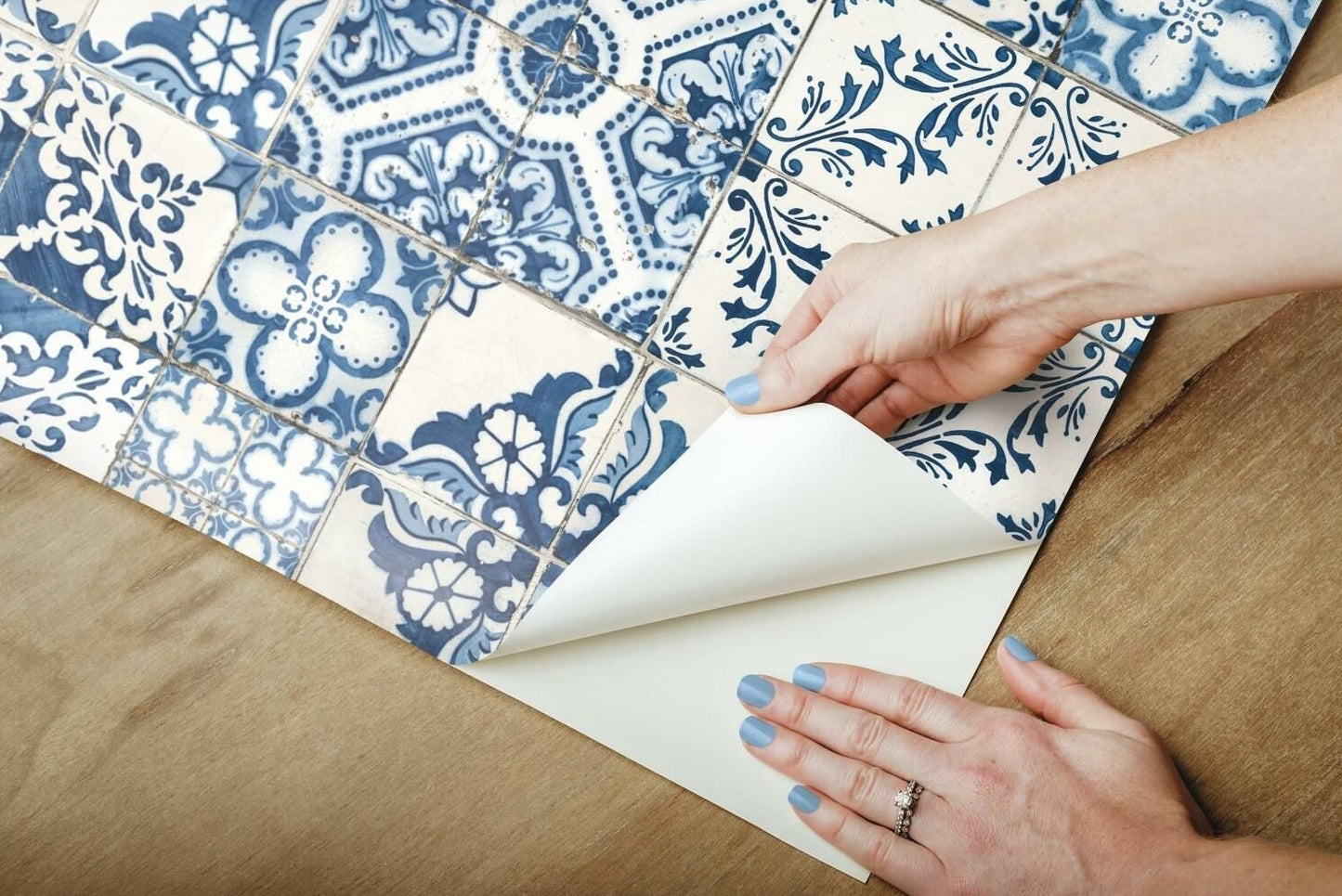 Hands applying blue and white Mediterranean style vinyl peel and stick wallpaper on wooden surface from home decor collection
