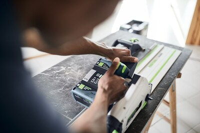 Person adjusting cordless Festool track saw with guide rail on workbench in home improvement workshop setting