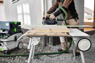 Person using a green power tool on a compact folding worktable in an outdoor woodworking tools setup