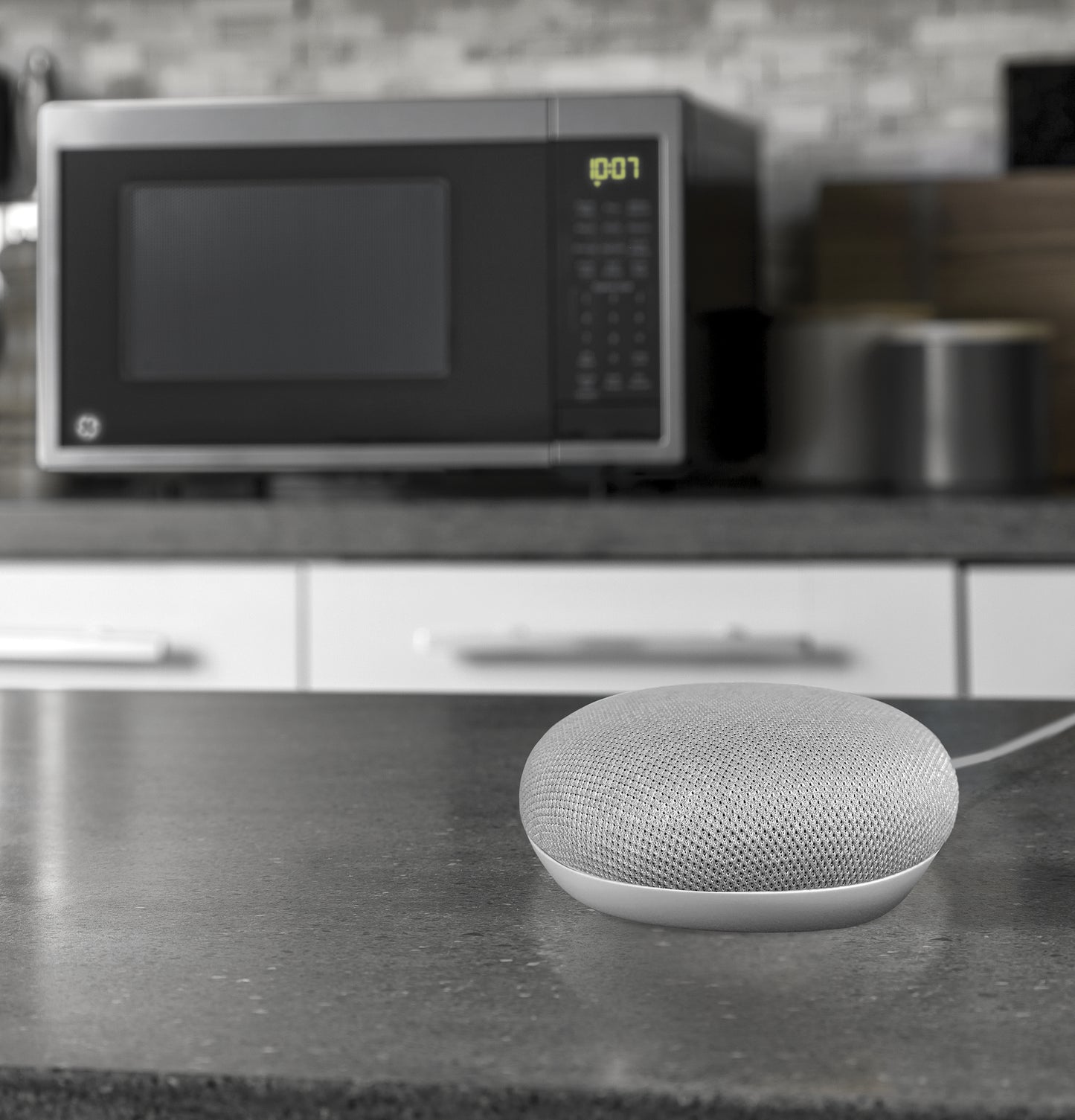 Smart speaker device on kitchen countertop with microwave oven and modern kitchen decor in background