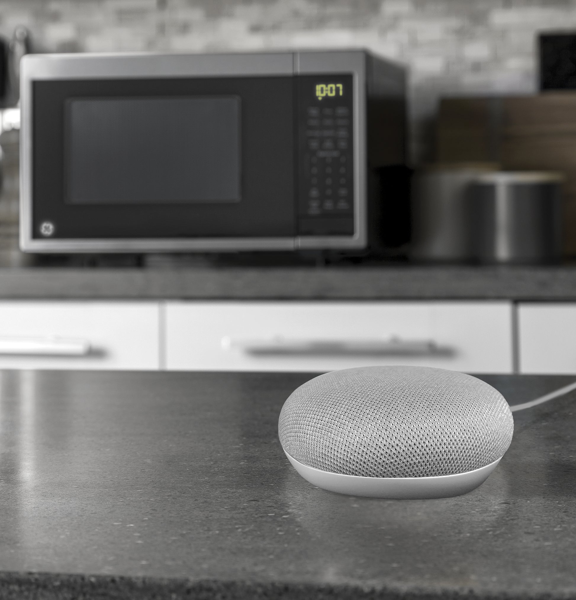 Smart speaker device on kitchen countertop with microwave oven and modern kitchen decor in background