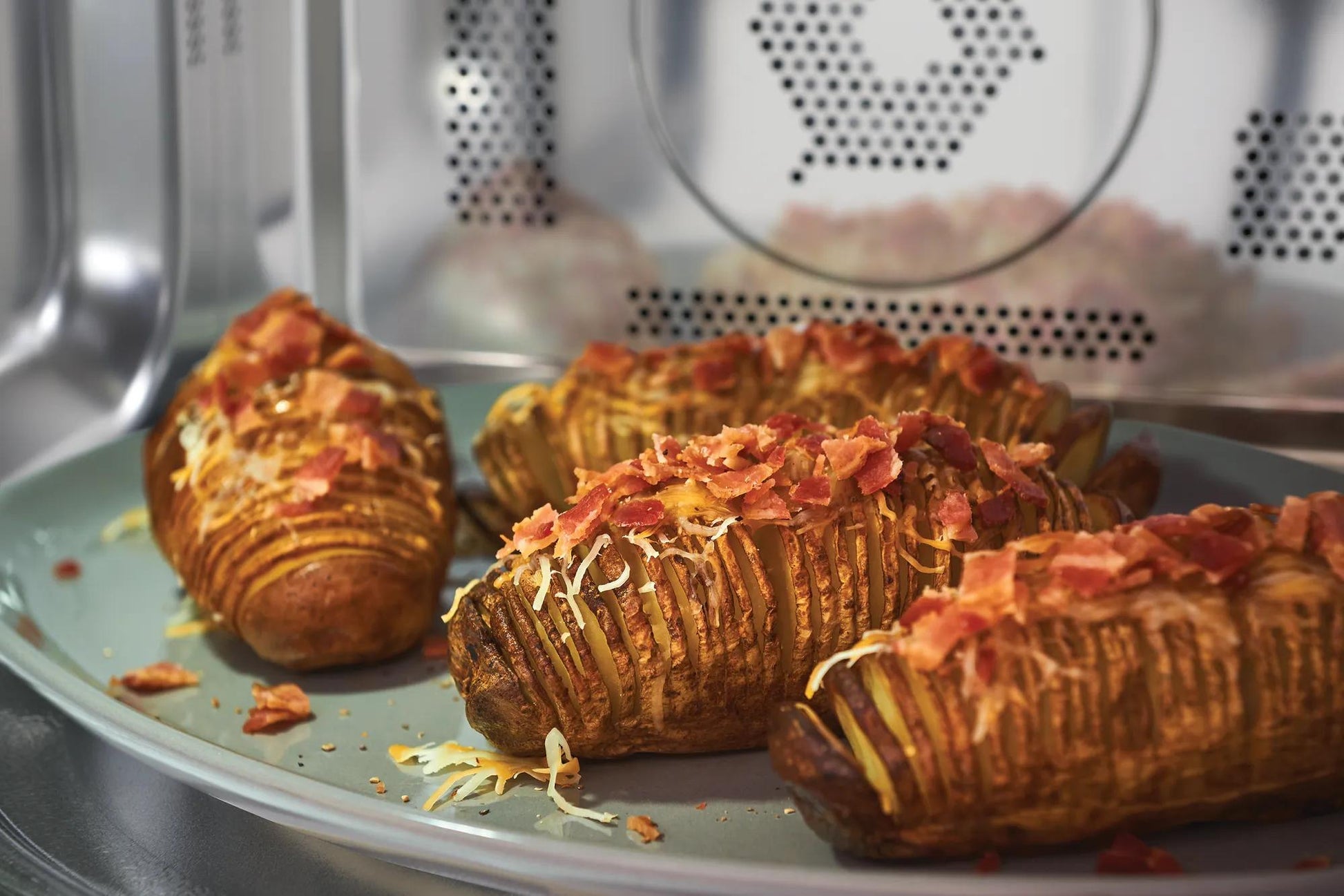 Close-up view inside built-in microwave with baked potatoes topped with melted cheese and bacon bits on plate