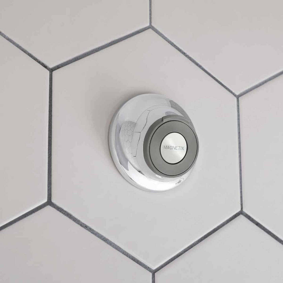 Chrome circular remote dock shower bracket with magnetic holder mounted on white hexagonal tiled wall