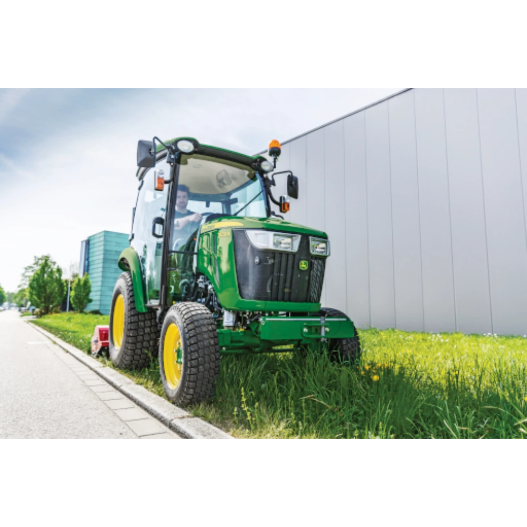 John Deere 3039R compact tractor with ComfortGard cab cutting grass along a roadside, featured in Outdoor Power Equipment at Hartville Hardware.