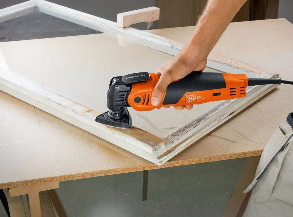 Orange and black Fein oscillating multitool sanding edge of old wooden window frame for home improvement tasks