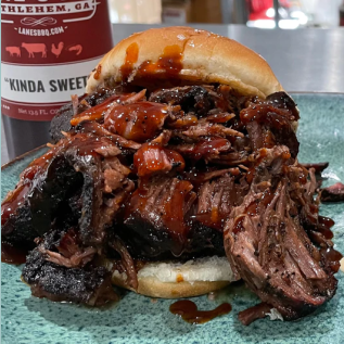 Pulled beef sandwich topped with smoky sweet barbecue sauce next to a bottle from grilling sauces and spices collections
