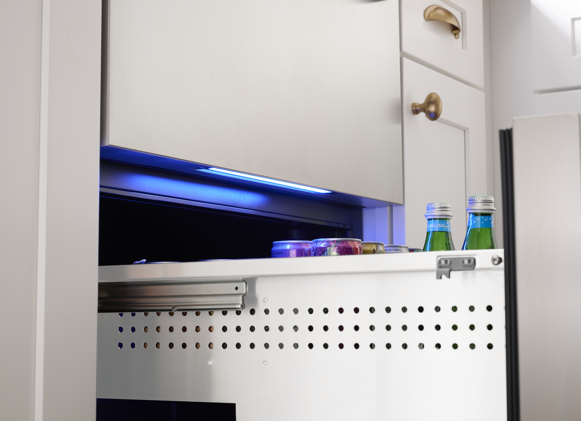 Under-counter stainless steel refrigerator drawer with interior blue LED light storing beverages in modern kitchen cabinetry