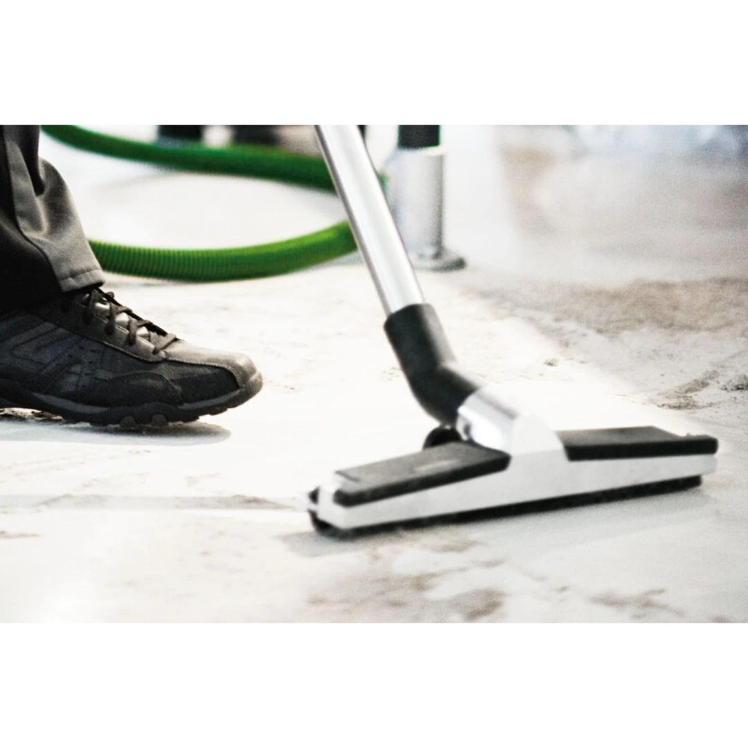 Aluminum industrial floor nozzle connected to vacuum hose cleaning concrete surface in home improvement setting
