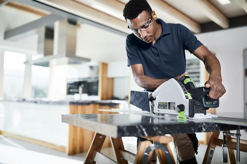 Man wearing safety glasses using cordless Festool track saw with guide rail for home improvement woodworking task