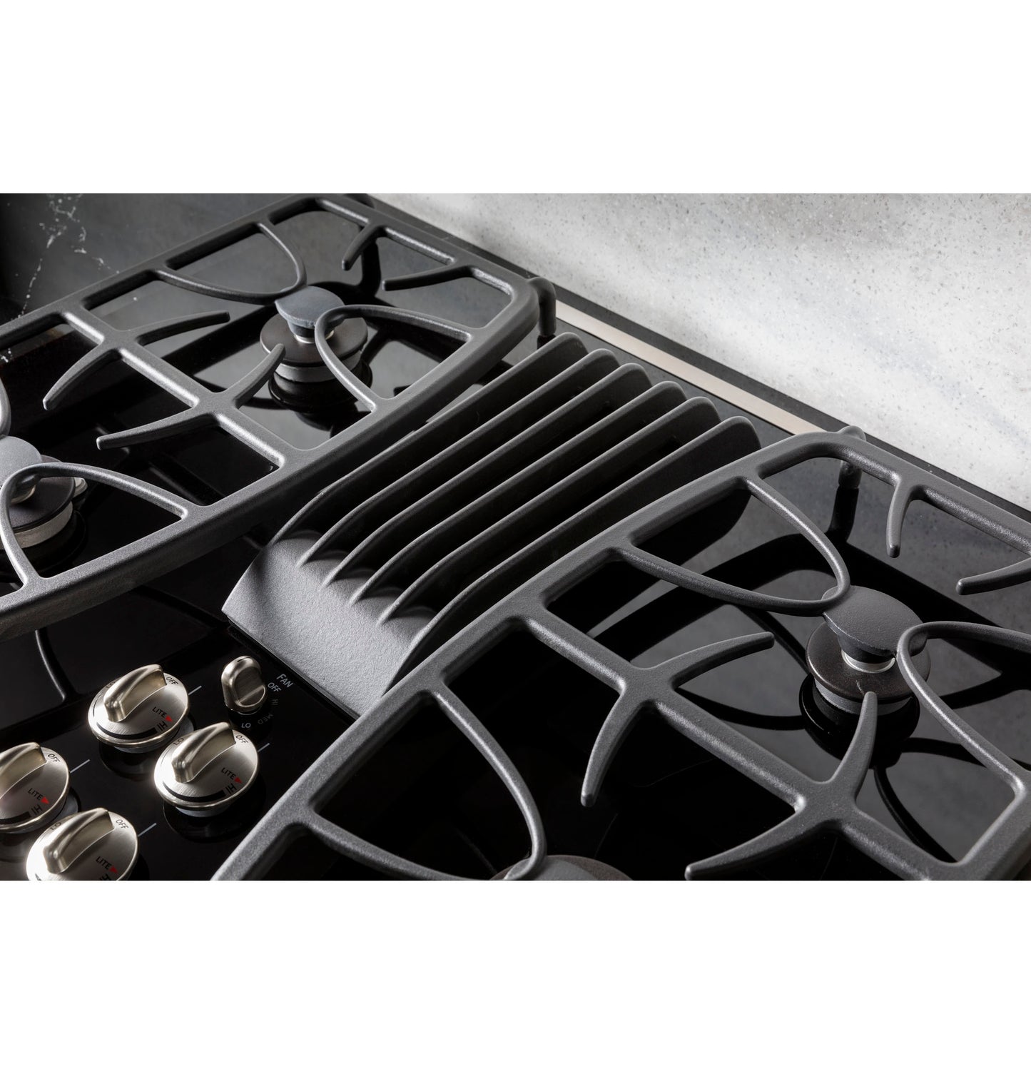 Close-up view of black built-in gas cooktop with downdraft vent and stainless steel control knobs in kitchen setting