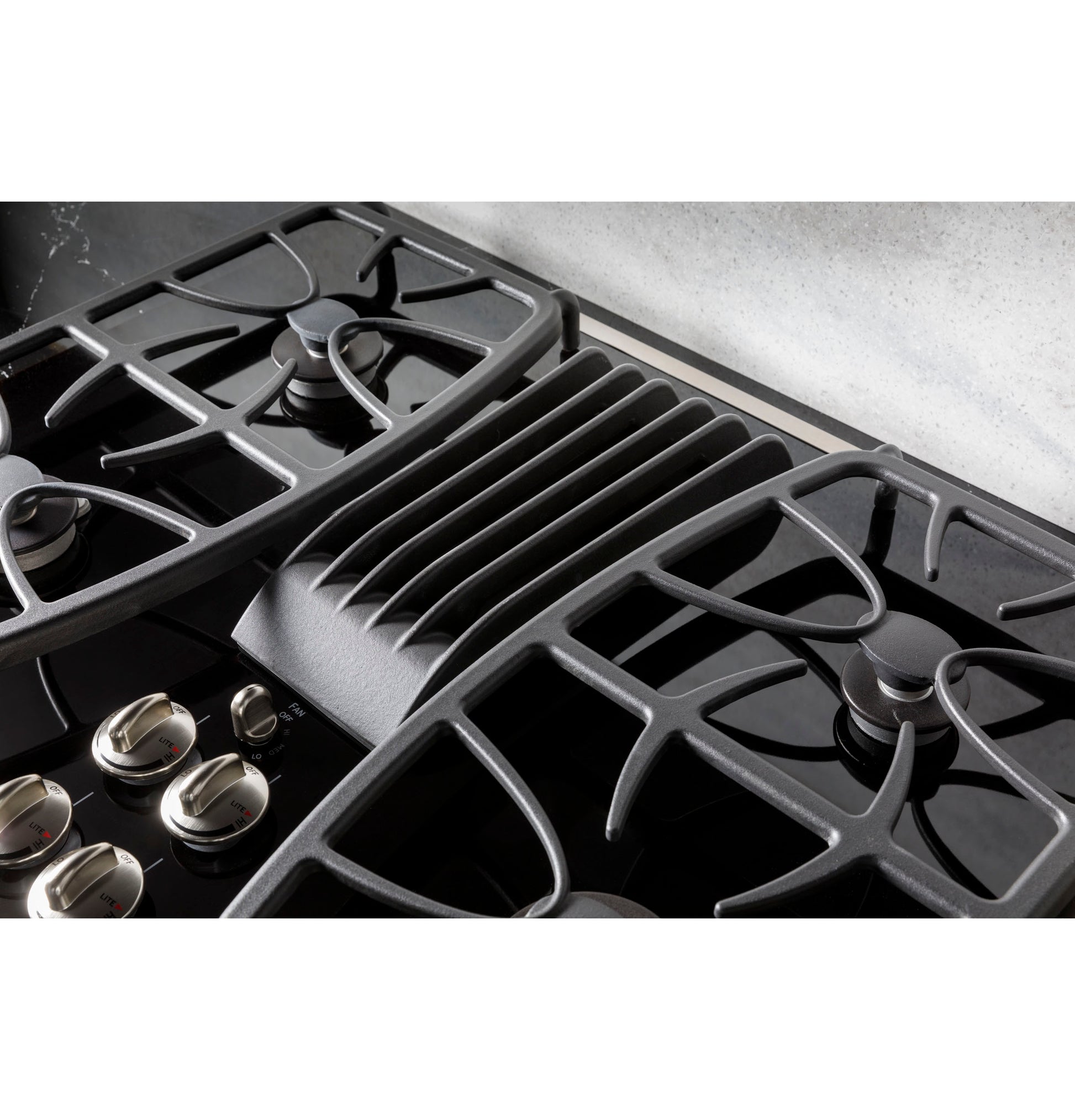 Close-up view of black built-in gas cooktop with downdraft vent and stainless steel control knobs in kitchen setting