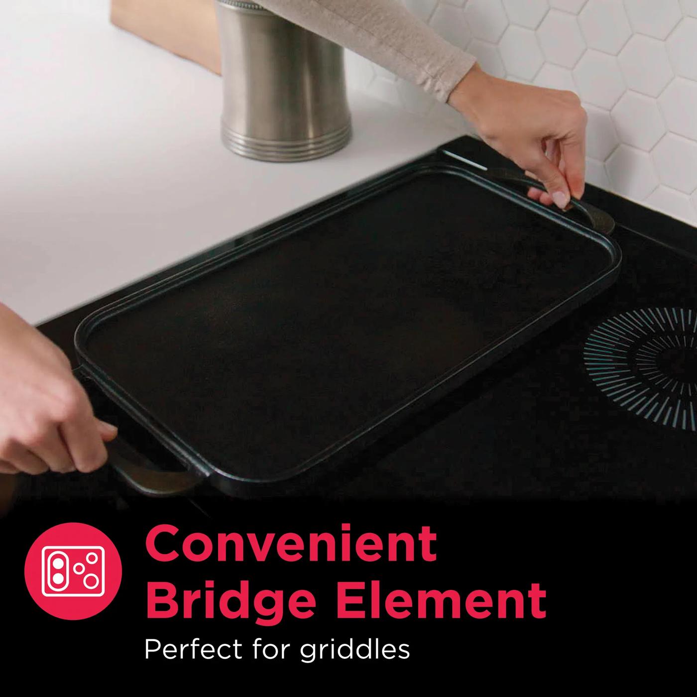 Person placing black rectangular griddle on induction cooktop featuring convenient bridge element for versatile cooking.