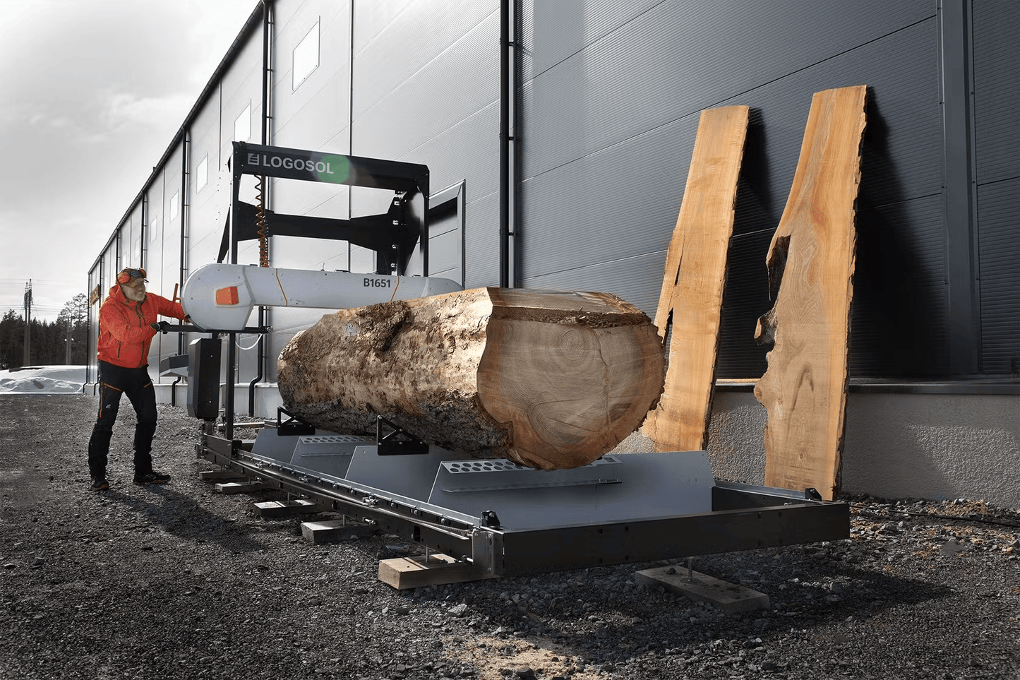Operator using a portable band sawmill with 27HP gasoline engine to cut a large log into lumber slabs outdoors