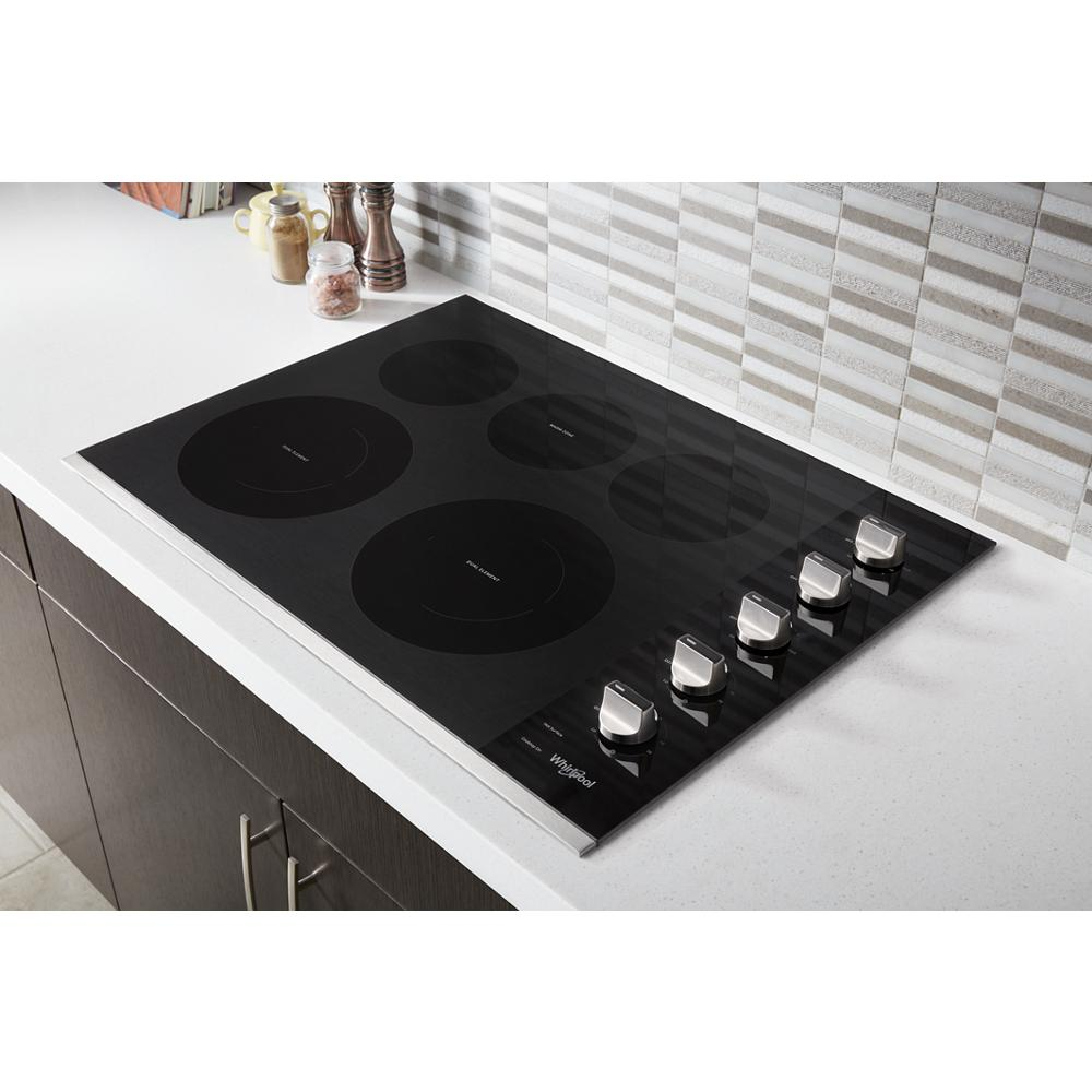 Black 30-inch electric ceramic glass cooktop with five burners and stainless steel control knobs in modern kitchen setting