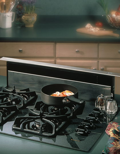 Black downdraft ventilation system installed behind a stovetop with cookware and kitchen accessories nearby