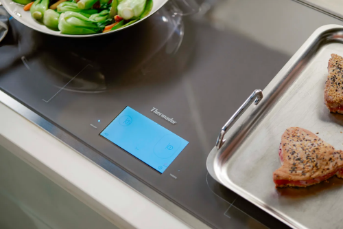 Dark gray induction cooktop surface mount with digital touch controls heating vegetables and meat in kitchen appliances collection