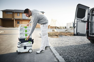 Worker loading white and green modular tool storage system into van for jobsite organization and workshop storage