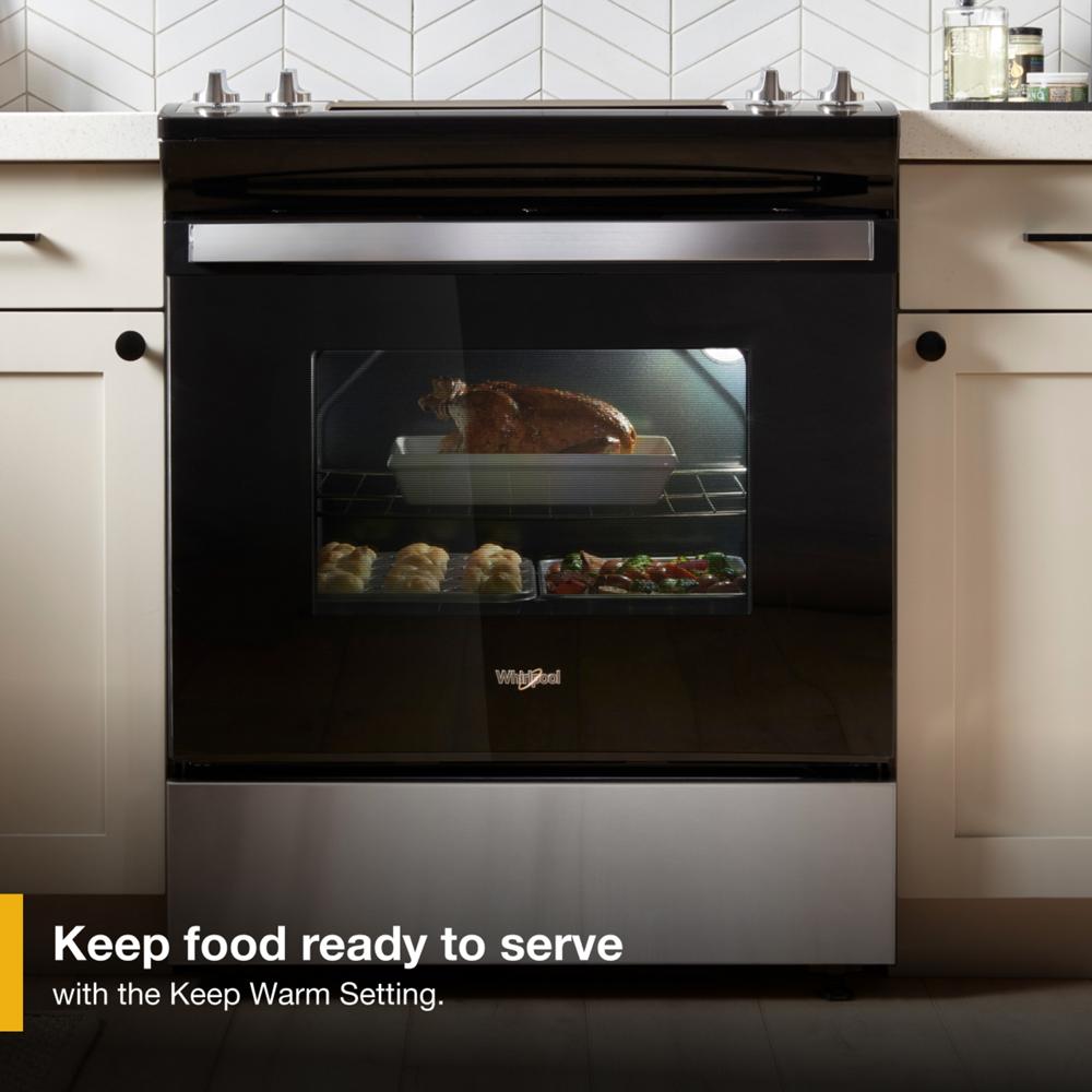 Black and stainless steel electric range with food roasting and baking inside visible through oven window in kitchen setting