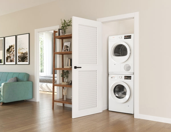 Stacked white compact front load washer and dryer set inside a small laundry closet with louvered door in modern home