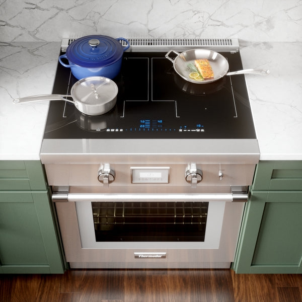 Stainless steel induction range with digital controls and cookware on black glass cooktop in kitchen setting