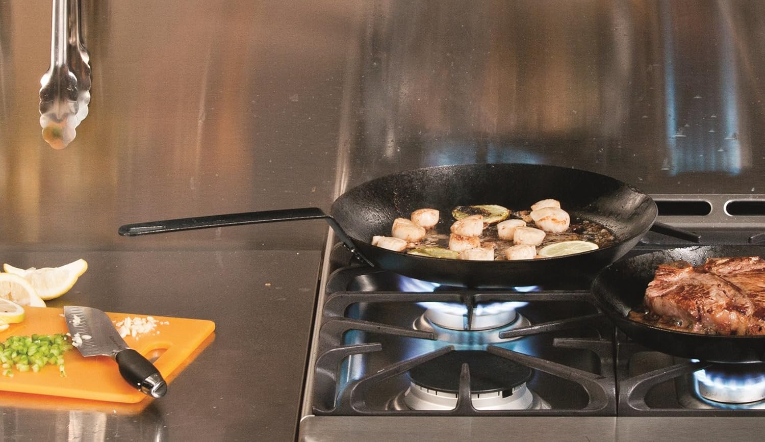Seasoned steel skillet sautéing shrimp and garlic on gas stove next to cast iron pan with steak in kitchenware collections