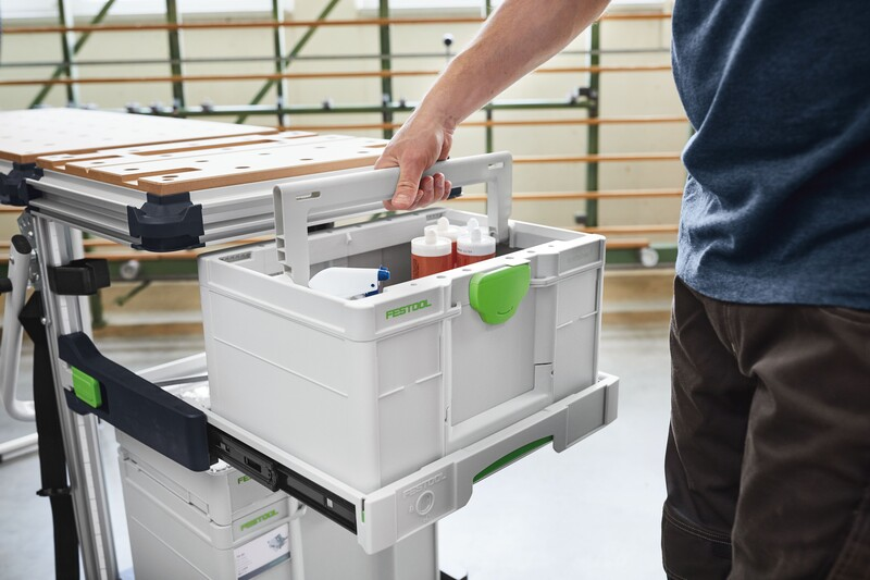 Person lifting white and green Festool pull-out drawer from mobile workcenter in workshop organization setting
