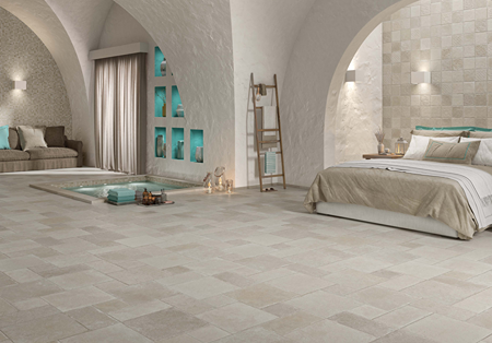 Spacious indoor room with matte tufo stone tiles, arched walls, and a neutral-toned bedroom and seating area flooring