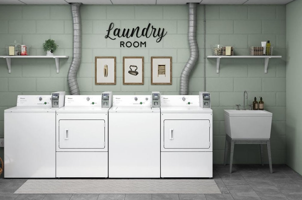 Row of white commercial top-load washers and dryers with coin slide controls in a modern laundry room setting