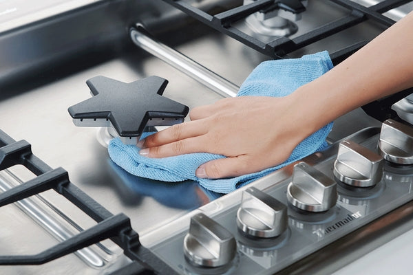 Hand wiping stainless steel gas cooktop surface with blue cloth, shown for kitchen and home improvement use