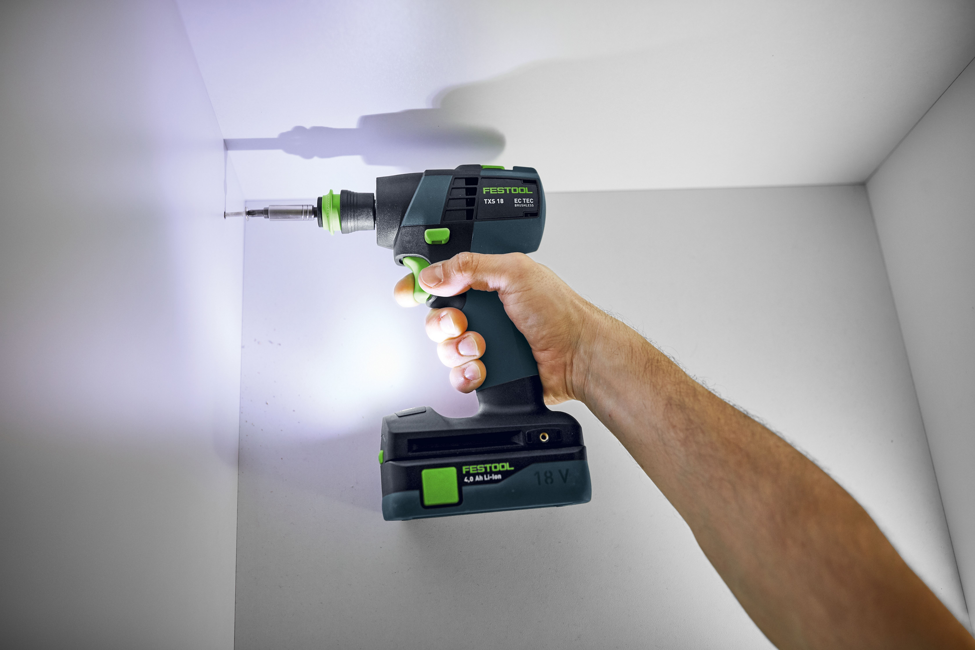 Cordless drill with LED light and ergonomic grip driving a screw in white interior corner for home improvement tasks