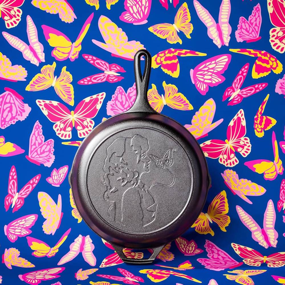 Cast iron skillet with embossed Dolly Parton profile and butterfly, placed on colorful butterfly patterned background, kitchenware collection