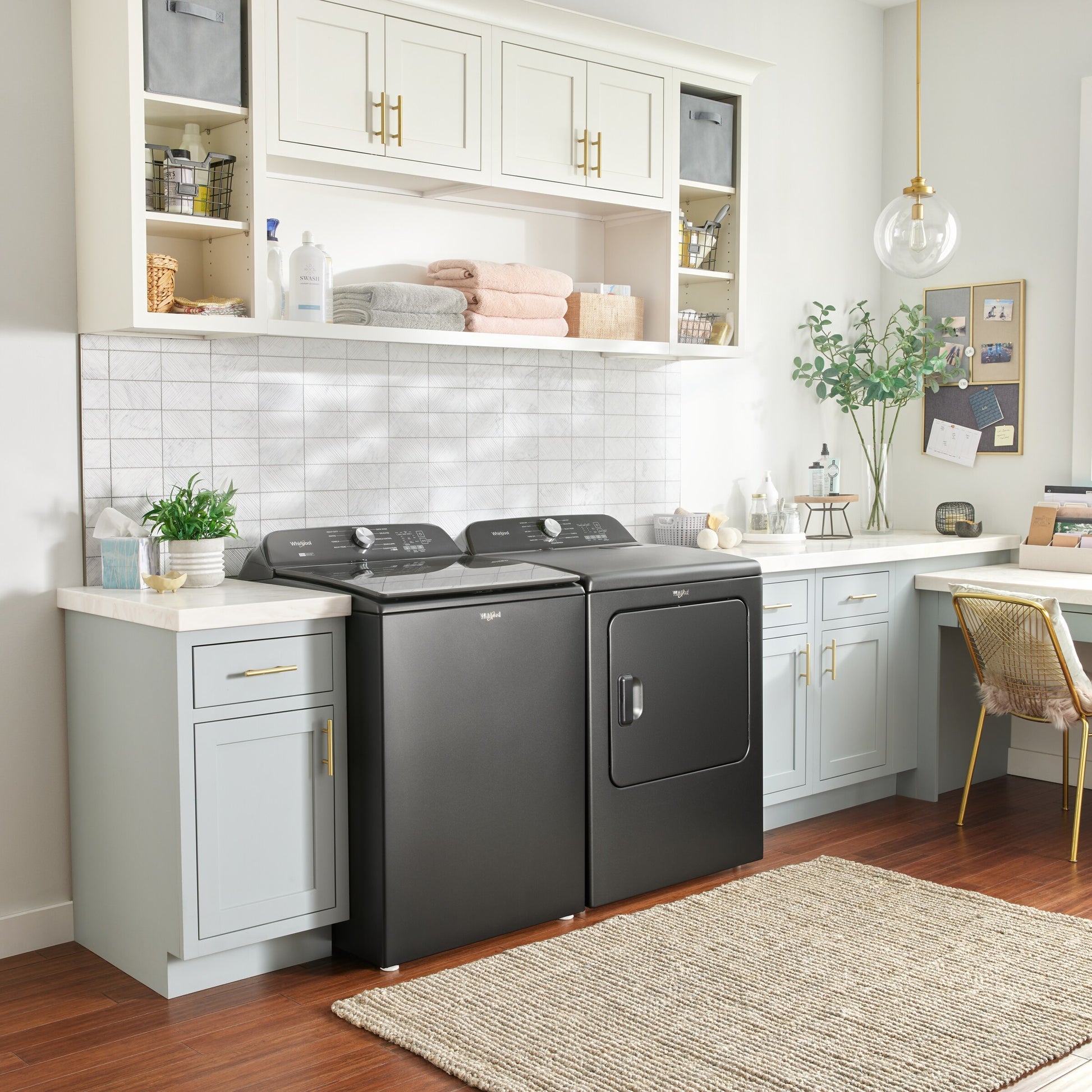 Modern black Whirlpool top load washer and matching dryer in stylish laundry room with built-in cabinets and home decor