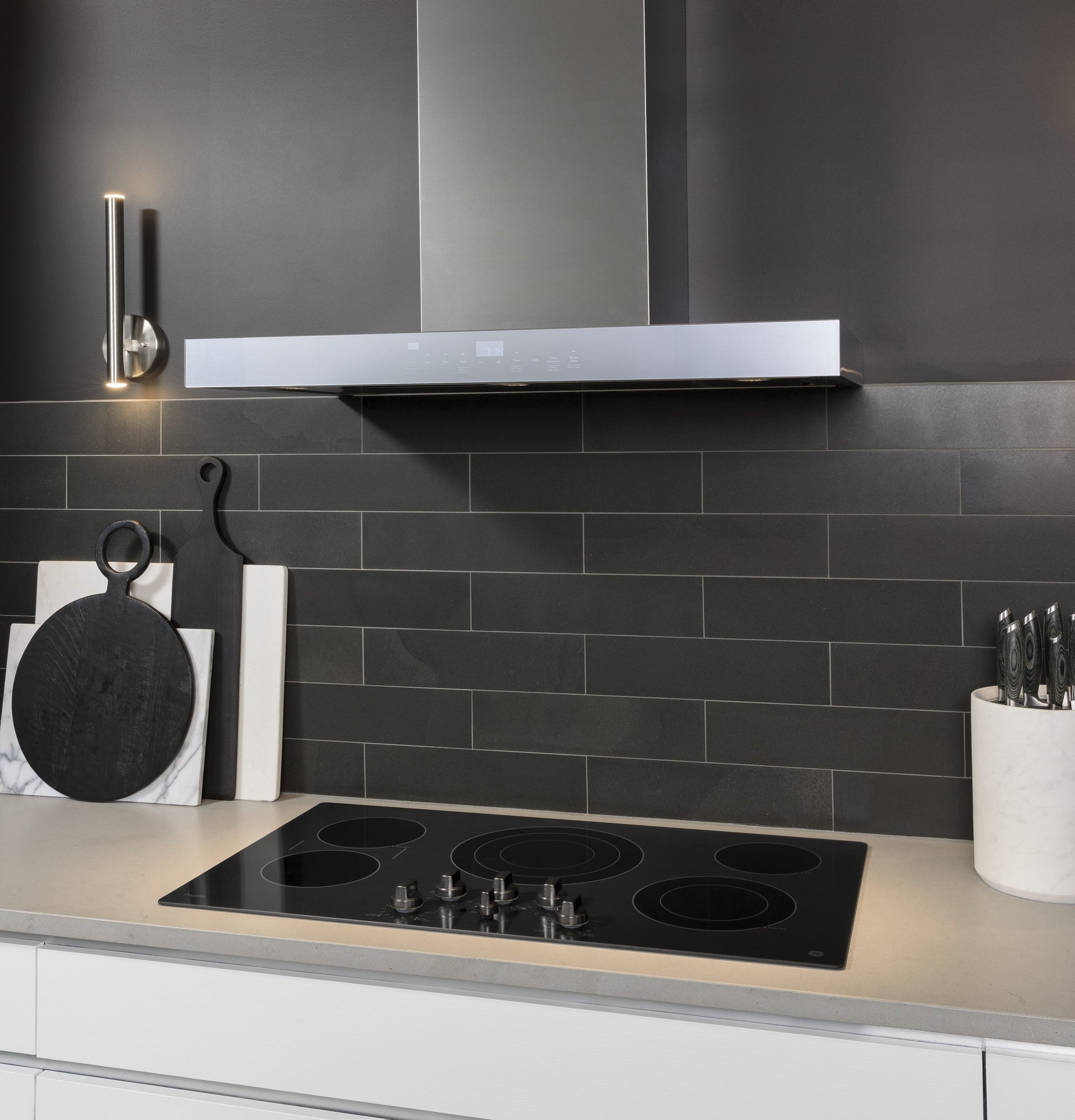 Sleek stainless steel wall mount range hood with perimeter venting above electric cooktop in modern kitchen setup
