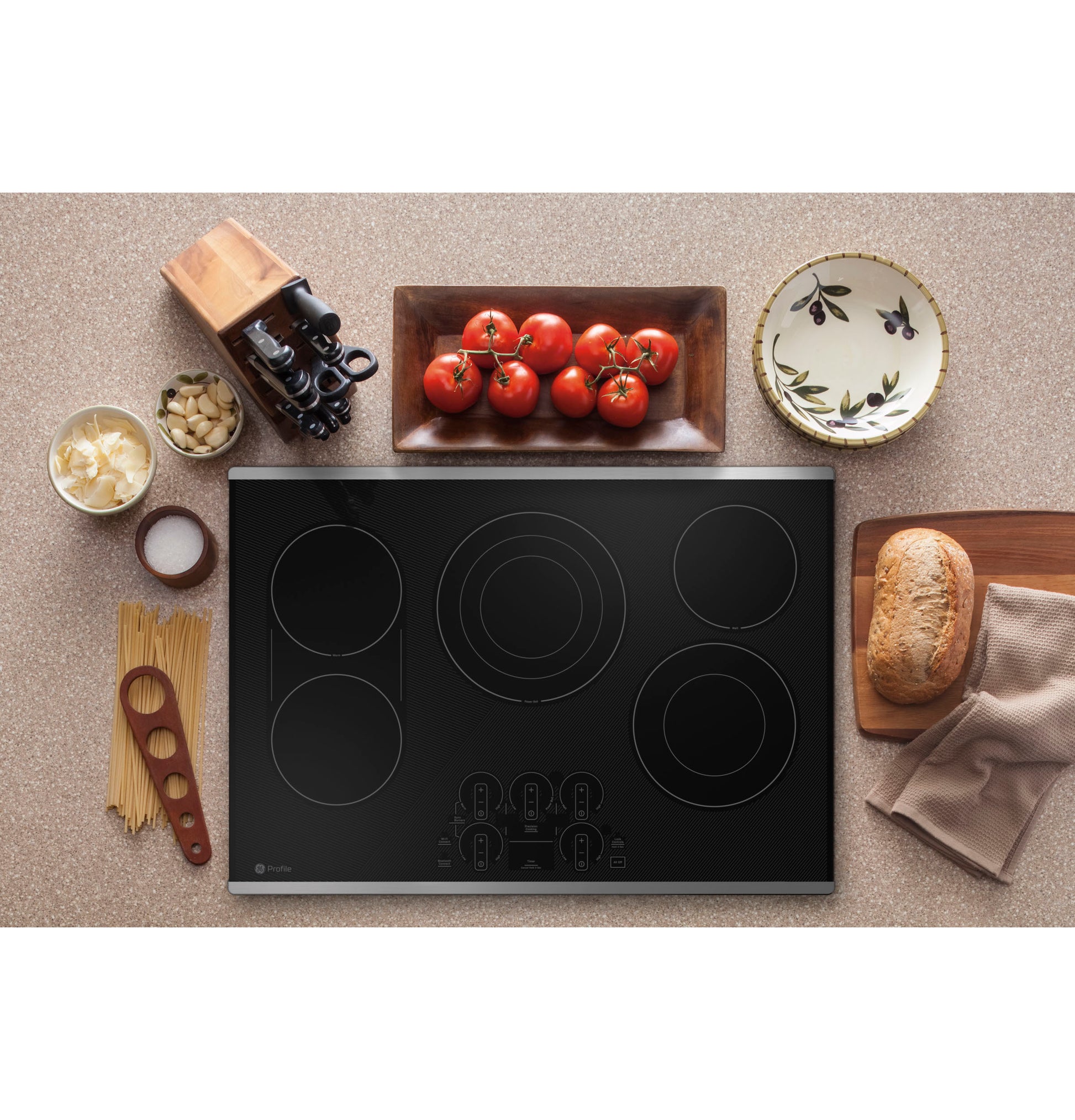 Black built-in electric cooktop with touch controls surrounded by cooking ingredients in kitchen setting