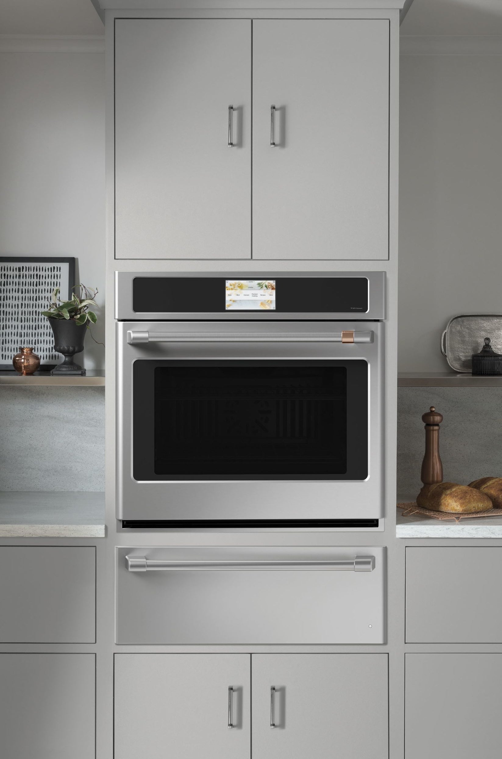 Modern built-in stainless steel wall oven with warming drawer integrated in light gray cabinetry from kitchen appliances collection