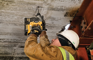 Worker in safety gear using a yellow DEWALT cordless rotary hammer drill on concrete ceiling for home improvement tasks