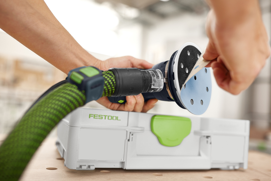 Person attaching circular sanding disc to a Festool random orbital sander with Festool storage box in background