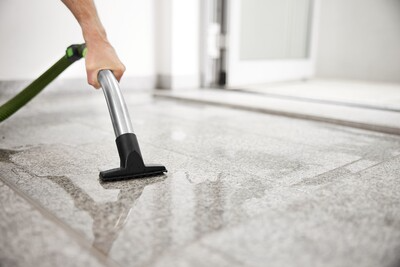 Hand using hose attachment from Festool dust extractor to clean water and debris from hard floor surface indoors