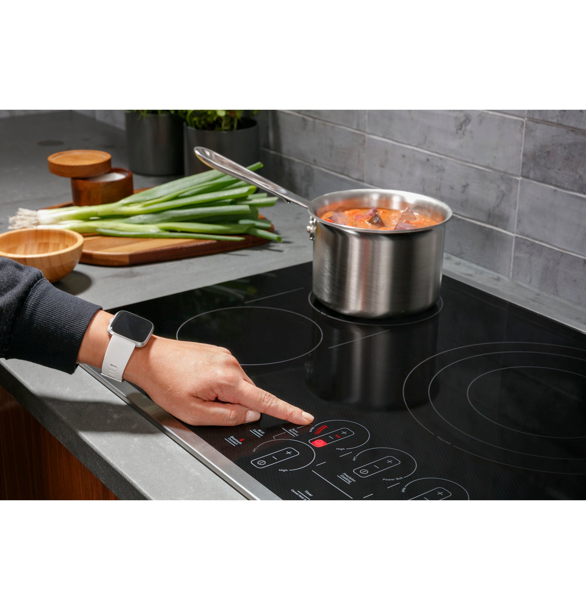 Person using touch controls on black electric cooktop with stainless steel pot and kitchen countertop in home improvement setting